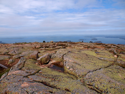 [Large broken rock expanses with islands in bay seen in the distance and clouds overhead.]